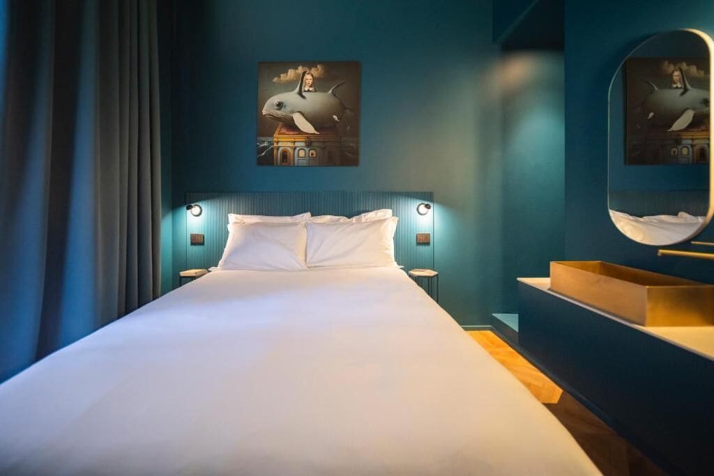 Una moderna camera d'albergo con un letto grande, un comodino, uno specchio e opere d'arte alle pareti.