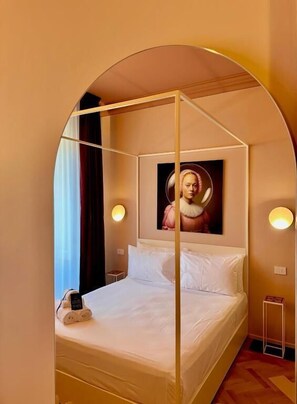 Een slaapkamer met een hemelbed, een schilderij van een vrouw en twee bedlampjes.