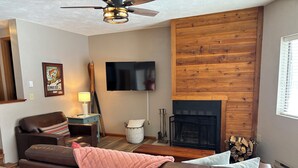 Ein Wohnzimmer mit braunem Ledersofa, einem an der Wand befestigten Fernseher, einem Kamin und einem Deckenventilator.