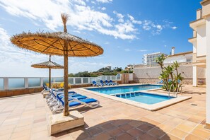 Ett poolområde på taket med solstolar och parasoller, en swimmingpool och utsikt över havet.