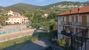 A residential area with a swimming pool, a building with a balcony, and a hilly landscape in the background. - Stella Marina: Three-Bedroom Apartment with Pool, 3 Balconies, and Free Parking (Pietra Ligure)