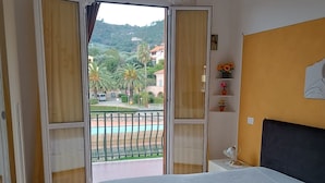 A bedroom with a bed, a view of a pool, and a balcony with curtains. - Stella Marina: Three-Bedroom Apartment with Pool, 3 Balconies, and Free Parking (Pietra Ligure)