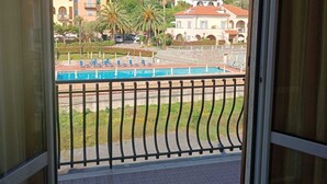 A balcony with a view of a pool, buildings, and a hilly landscape. - Stella Marina: Three-Bedroom Apartment with Pool, 3 Balconies, and Free Parking (Pietra Ligure)