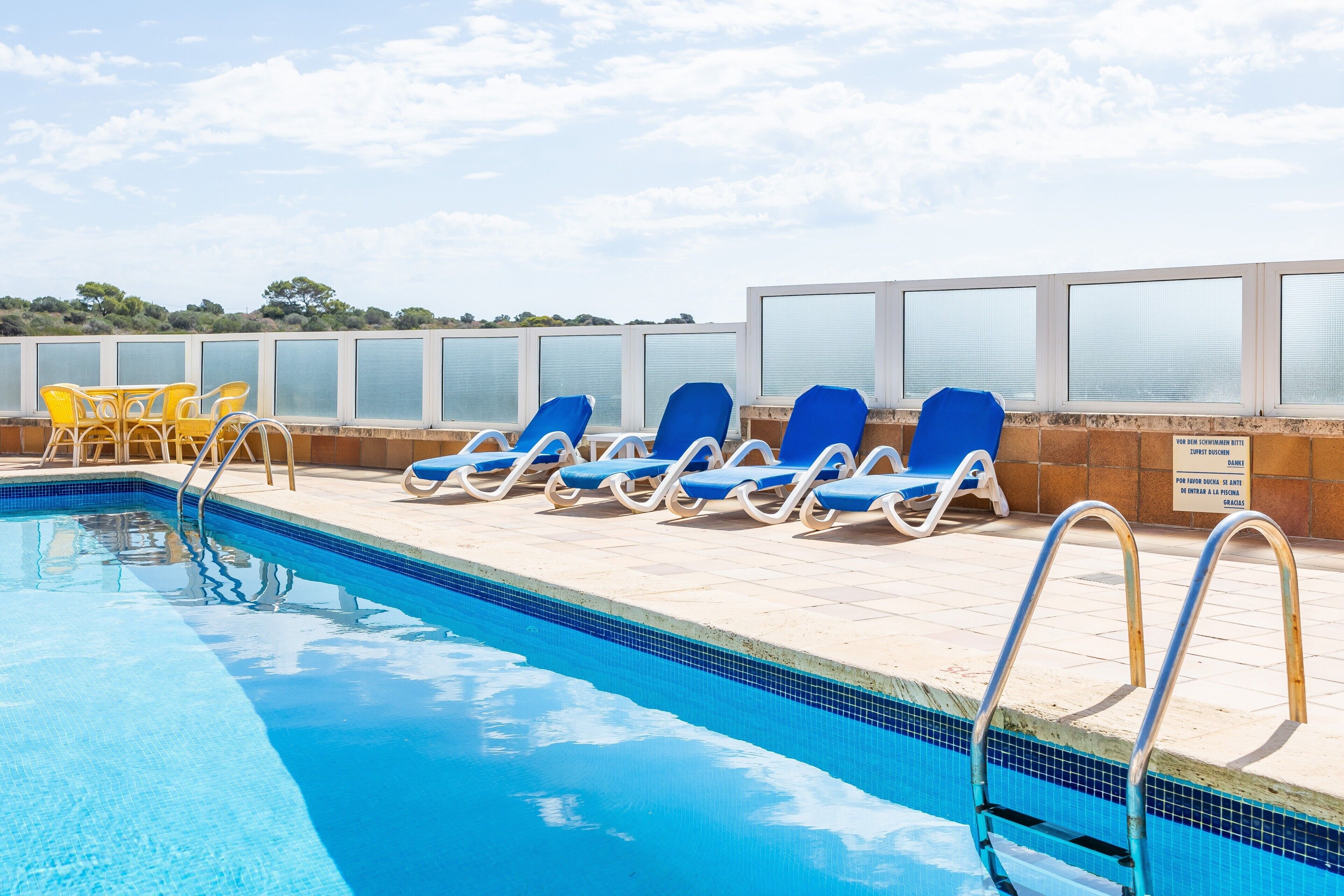 Une piscine à l’eau bleue, entourée de chaises longues et dotée d’une balustrade en verre.