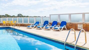 Une piscine à l’eau bleue, entourée de chaises longues et dotée d’une balustrade en verre.