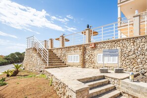 A stone building with a staircase leading to a balcony, a sign indicating a private pool, and a clear sky. - Apartment 'Aptos Villa Sirena Vista Mar' with Shared Pool, Wi-Fi and Air Conditioning (Cala Figuera)