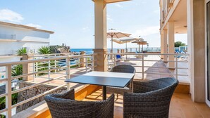 Ein Balkon mit Korbstühlen und einem Tisch, der Blick auf einen Pool und das Meer freigibt.