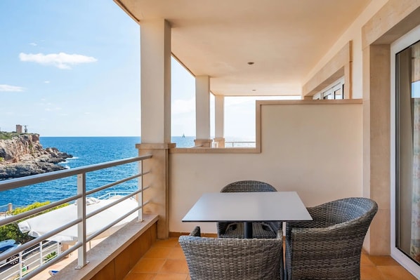 Un balcon avec une table et des chaises, donnant sur une côte rocheuse et la mer.