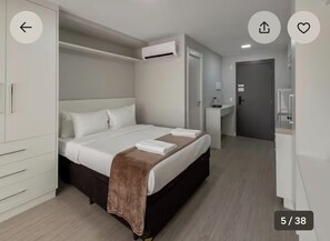 Een moderne hotelkamer met een groot bed, een kledingkast, een airconditioning en een badkamer met spiegel en wastafel.