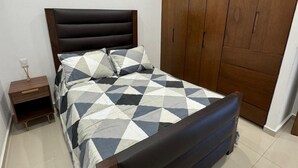 Een slaapkamer met een bed, nachtkastje, kledingkast en betegelde vloer.