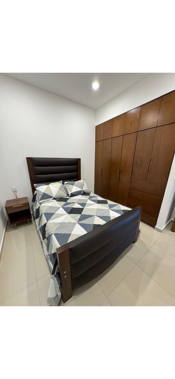 Une chambre à coucher comprenant un lit, une table de chevet, une armoire et un sol carrelé.
