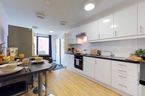 A modern kitchen with white cabinets, a black countertop, and stainless steel appliances. There is a dining area with a table and chairs, and a window providing natural light.
