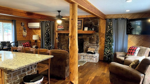 A cozy cabin interior with a stone fireplace, wooden beams, and a stone wall.