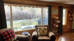 A cozy room with a large window, a wooden interior, a fireplace, and a seating area with a table and chairs.