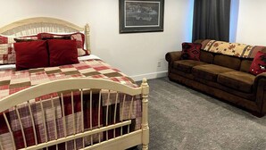 A bedroom with a bed, a wooden headboard, a framed picture on the wall, a brown sofa, and a window with curtains.