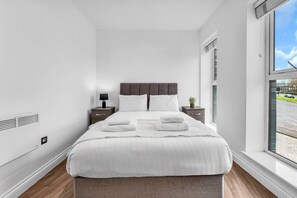 A hotel room with a large bed, a bedside table with a lamp, a small plant, and a window with a view of the street. - Modern 2‑Bed Apt | Contractor Friendly | Parking (Birmingham)