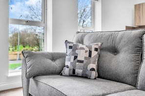 A grey upholstered sofa with a geometric patterned pillow in a room with large windows. - Modern 2‑Bed Apt | Contractor Friendly | Parking (Birmingham)
