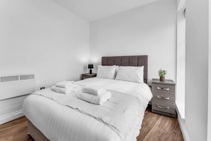 A modern bedroom with a bed, bedside tables, and a small plant. - Modern 2‑Bed Apt | Contractor Friendly | Parking (Birmingham)