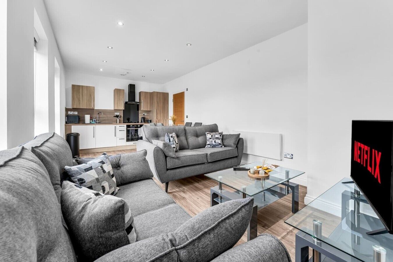A modern living room with a grey sofa, a glass coffee table, and a flat-screen TV displaying the Netflix logo.
