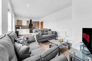 A modern living room with a grey sofa, a glass coffee table, and a flat-screen TV displaying the Netflix logo. - Modern 2‑Bed Apt | Contractor Friendly | Parking (Birmingham)
