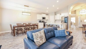 Uma sala de estar moderna com um sofá de couro azul, área de jantar com cadeiras de madeira e cozinha com armários brancos e eletrodomésticos de aço inoxidável.