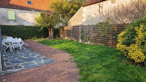 Un edificio in pietra con tetto a tegole, un vialetto sterrato e un'area verde delimitata da una recinzione in legno.