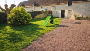 Un cortile con un vialetto sterrato, uno scivolo verde e un’altalena.