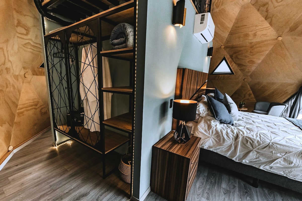 A modern bedroom with a loft-style bed, built-in shelving, and a small bedside table.