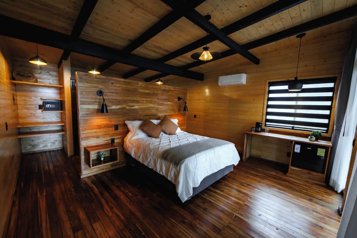 A wooden cabin interior with a bed, shelves, and a desk area.