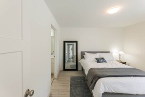 A bedroom with a bed, bedside table, lamp, and a mirror. - Red Sand Roost - Stratford Duplex Minutes from Beach and Charlottetown (Stratford)
