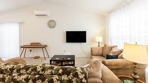 Ein Wohnzimmer mit einer Couch, einem Couchtisch, einem an der Wand montierten Fernseher und einer Lampe.