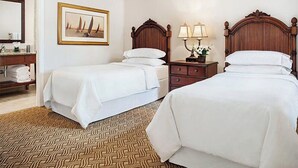 Habitación de hotel con dos camas, un cabecero de madera, una mesita de noche con lámparas, un cuadro enmarcado en la pared y una alfombra estampada.
