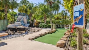 Campo de golf con un green, una valla de madera y un cartel.