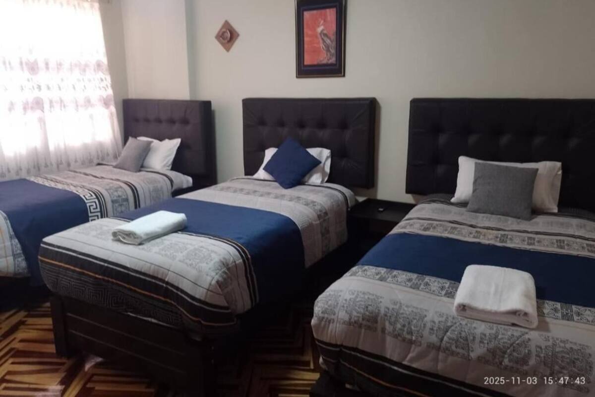 Une chambre d’hôtel avec trois lits, chacun doté d’une tête de lit et d’oreillers, et un plancher en bois.
