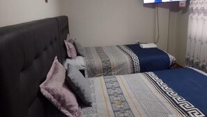 A bedroom with two beds, a television mounted on the wall, and a decorative wall piece. - HOTEL SAN ANTONIO  (Puno)