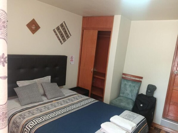 A bedroom with a bed, a wardrobe, a chair, and a suitcase. - HOTEL SAN ANTONIO (Puno)