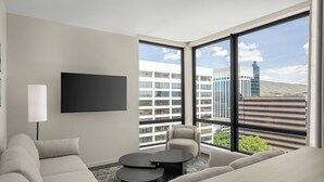 Une chambre d’hôtel moderne dotée d’une grande fenêtre, d’un téléviseur à écran plat, d’un canapé, d’un fauteuil et d’une petite table basse.