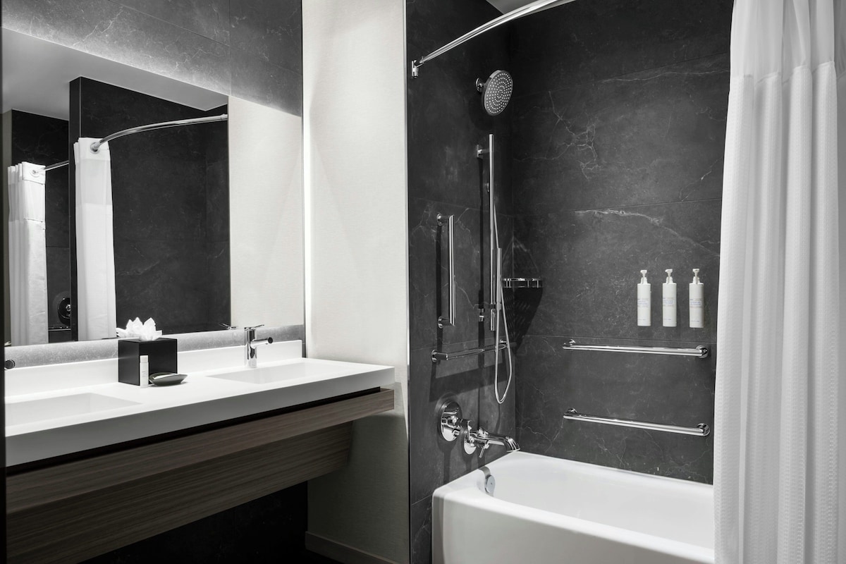 Une salle de bain moderne dotée d’un grand miroir, d’une baignoire, d’une zone de douche et d’un meuble-lavabo avec un évier.