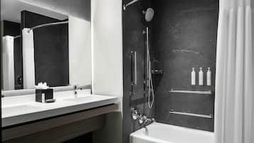A modern bathroom with a large mirror, a bathtub, a shower area, and a vanity with a sink.