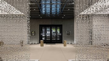Entrada d'hotel de disseny modern, amb una porta de vidre i una paret metàl·lica amb ornaments penjants.