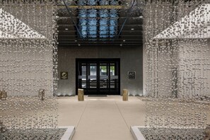 L’entrée d’un hôtel au design moderne, avec une porte en verre et un mur métallique orné de décorations suspendues.