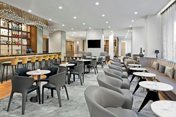 Eine moderne Hotelhalle mit Barbereich, Sitzgelegenheiten und einem großen Fernsehbildschirm.