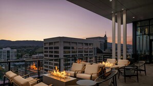 Une terrasse sur le toit, dotée d’un espace extérieur aménagé et d’un foyer, offrant une vue sur le paysage urbain au crépuscule.