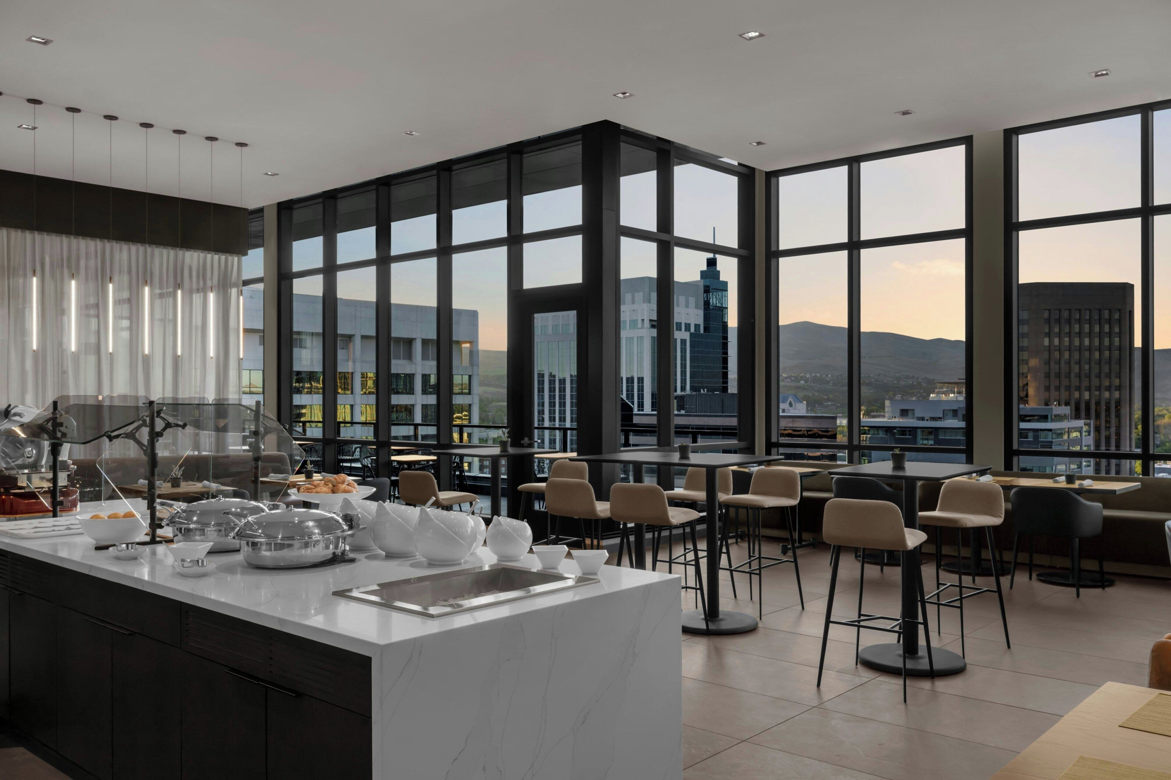 A modern dining area with a large window view, a central island with kitchen appliances, and multiple seating options.