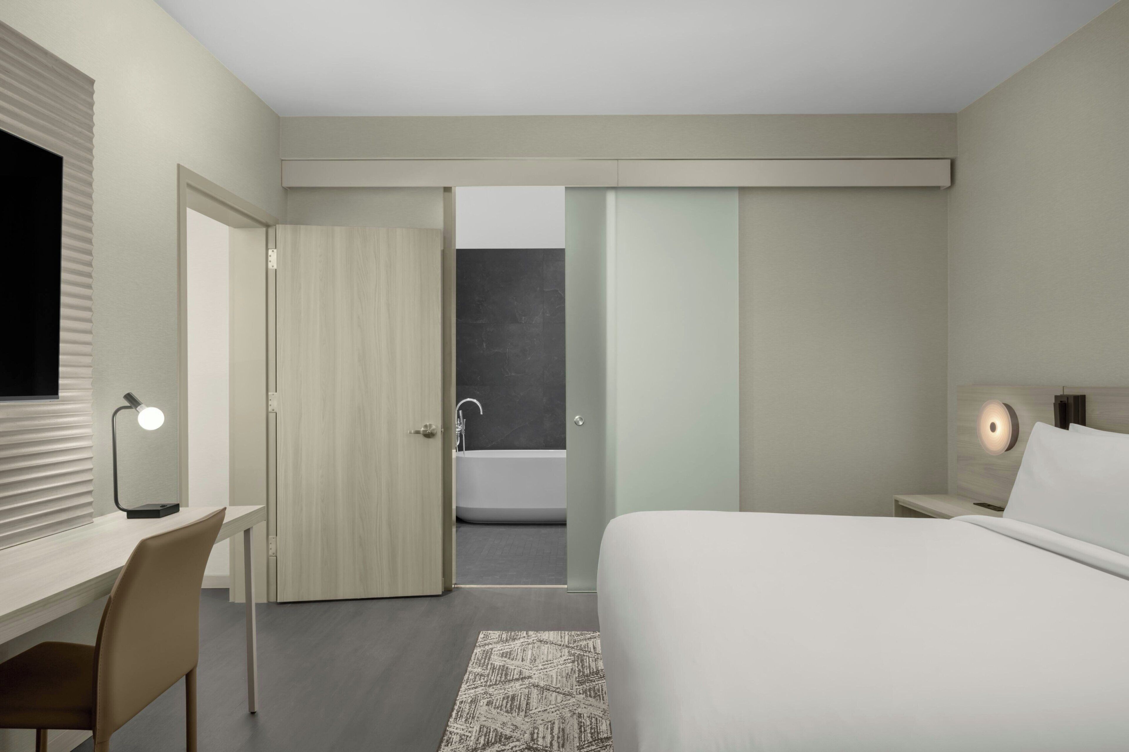Habitació d'hotel moderna amb llit, escriptori, cadira i bany amb banyera i dutxa.