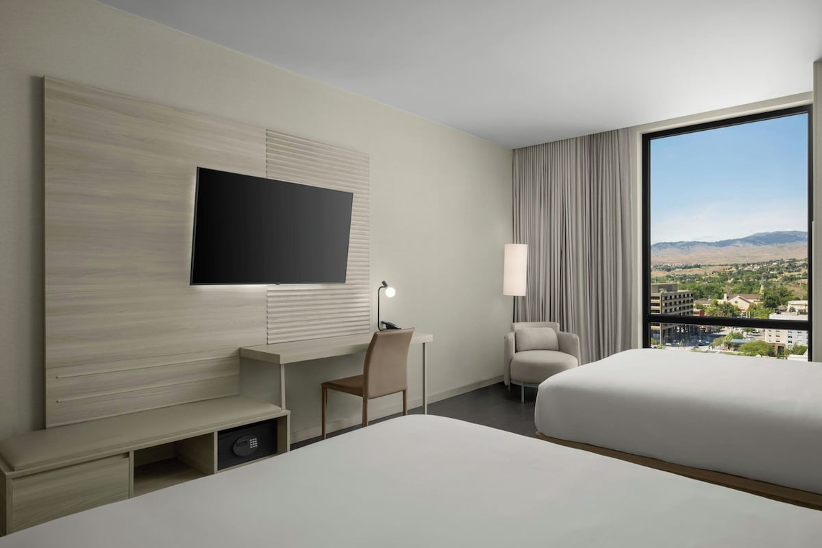 Une chambre d’hôtel équipée d’un lit, d’un bureau, d’une chaise, d’une télévision et d’une grande fenêtre donnant sur la ville.
