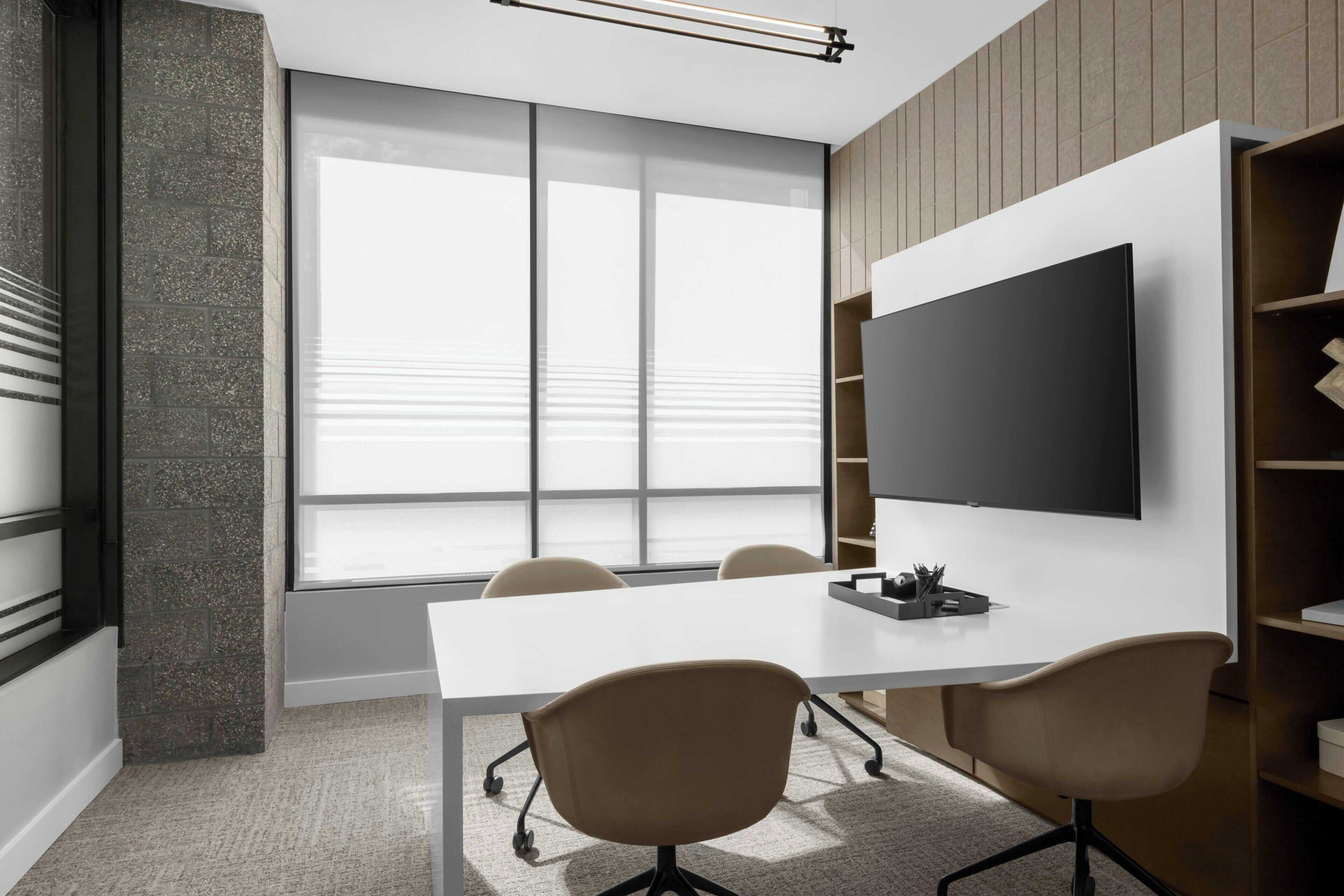 A modern conference room with a large flat-screen TV, a white table, and four chairs.