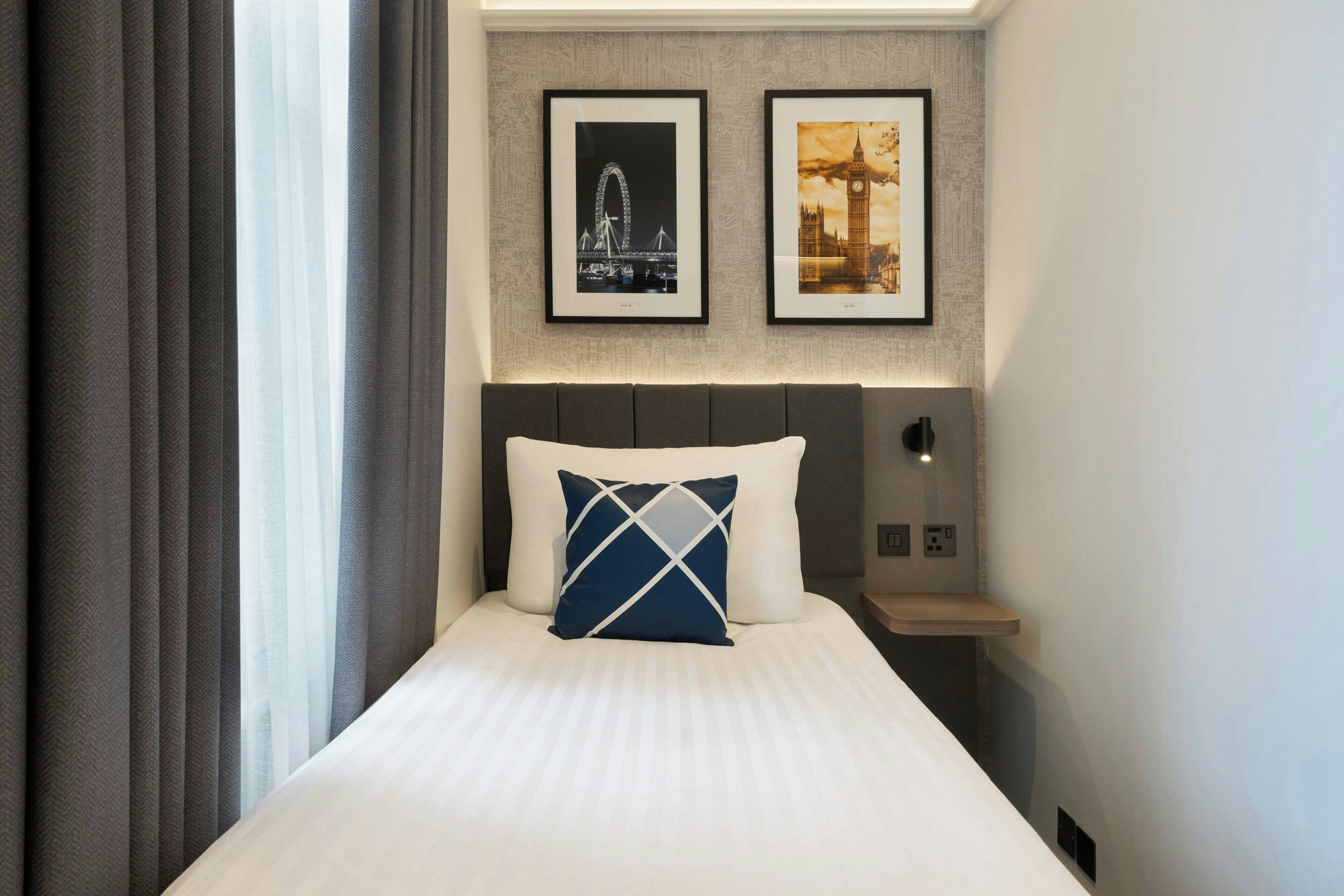 Una habitación de hotel con una cama, una mesita de noche y dos cuadros en la pared.