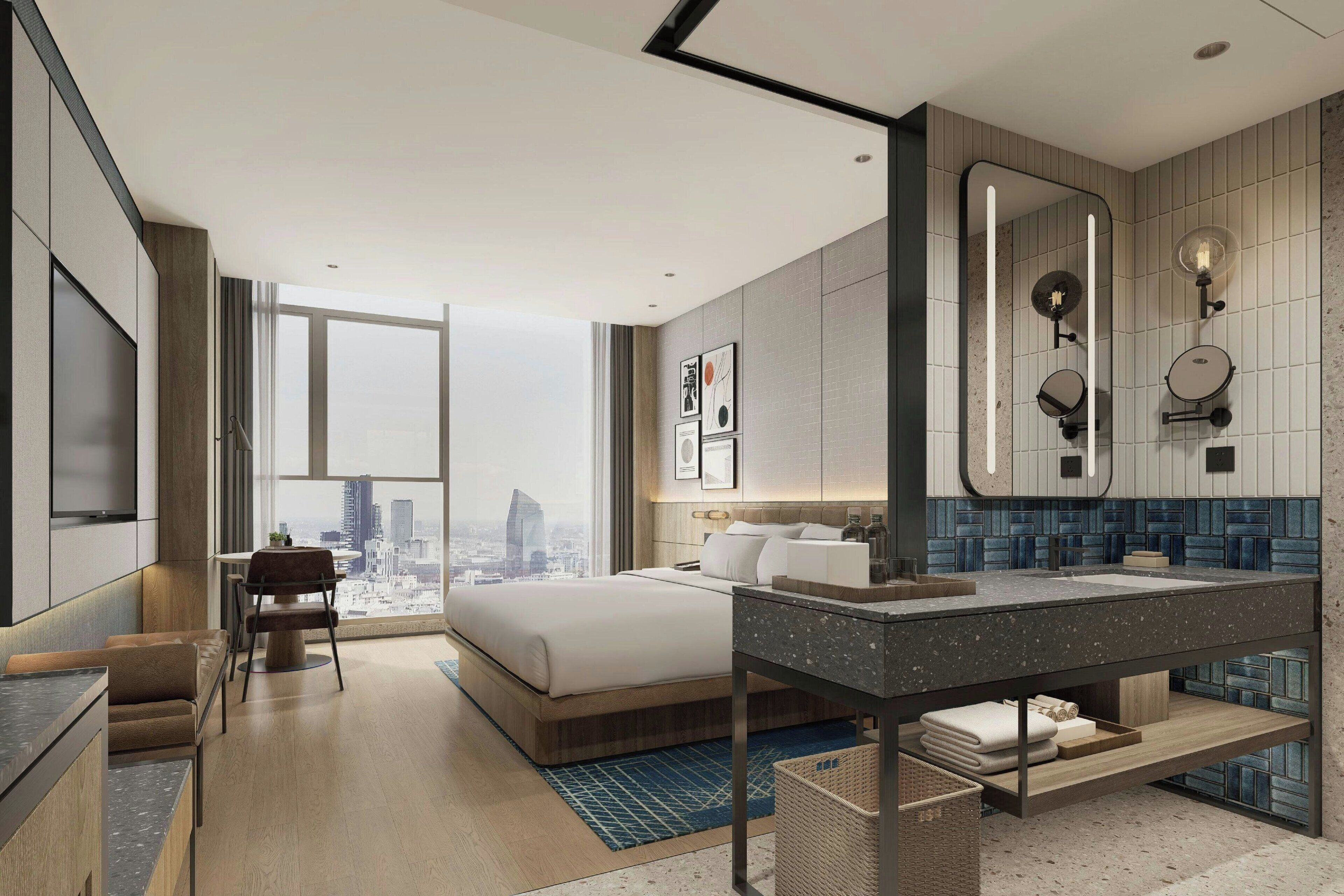 Una habitación de hotel moderna con una cama grande, un área de descanso, un baño con un espejo amplio y vistas a la ciudad.
