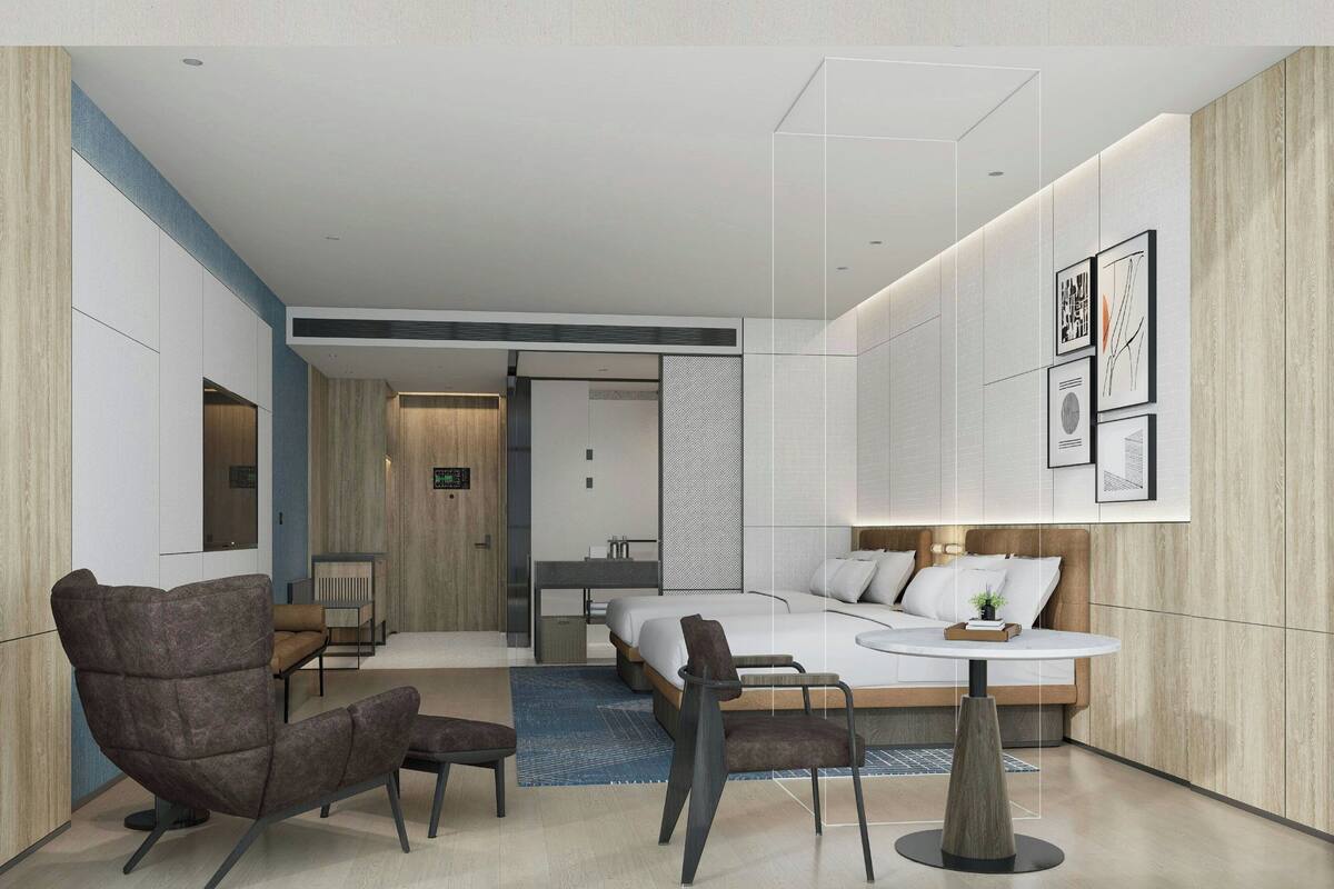 A modern hotel room with a bed, two armchairs, a small table, and a desk.